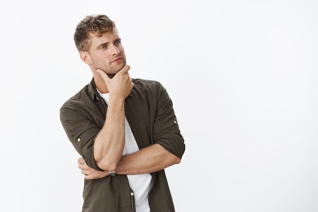 Skillful and thoughtful good-looking husband planning how put furniture looking and turning right rubbing bristle as thinking, making decision or choice in supermarket over white wall.