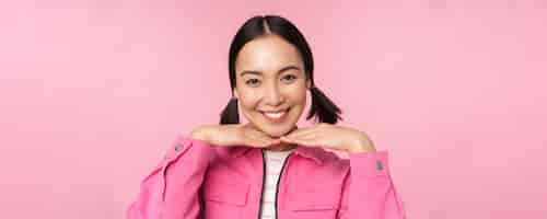 Free photo skin care and cosmetology concept beautiful asian girl smiling and laughing showing clean healthy facial skin posing against pink background copy space