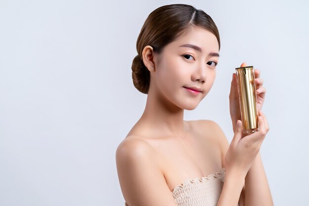 Skincare and makeup concept beautiful asian female woman with healthy facial skin close up portrait studio shot hand hold serum pr cream package with happiness and joyful