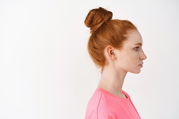 Skincare and makeup concept Profile of young woman with natural red hair combed in messy bun looking right standing over white background Facial treatment