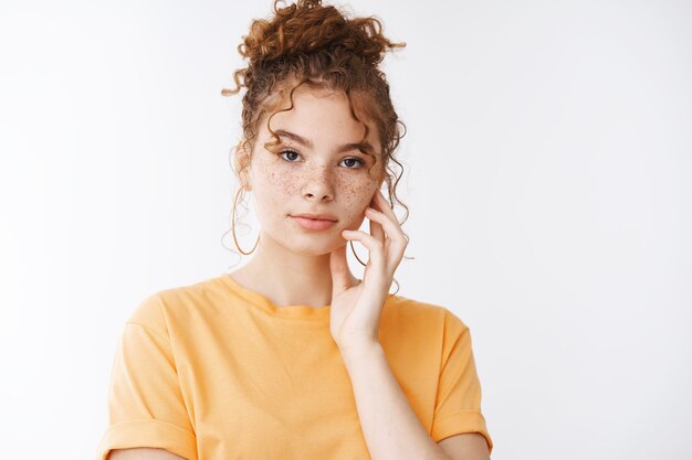 Skincare, tenderness fashion concept. Sensual attractive redhead girl freckles curly hairbun wear orange t-shirt look camera touch pure gentle skin applying cosmetic product, white background