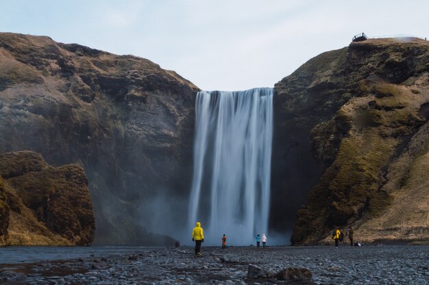 Skogafoss waterfall surrounded by people and rocks under a cloudy sky in iceland