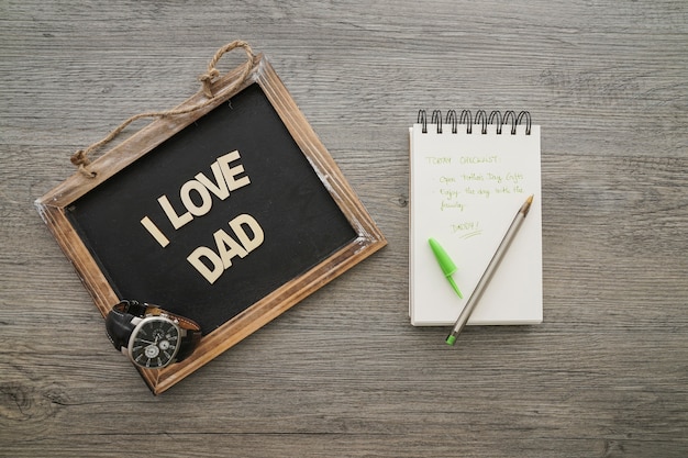 Free photo slate, watch and notebook on wooden surface for father's day