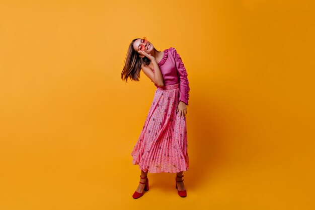 Slavic model with dark short hair moving on orange wall posing. Extraordinarily beautiful woman in dark pink look