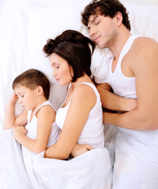 Sleeping family with little child lying on a bed. High angle view