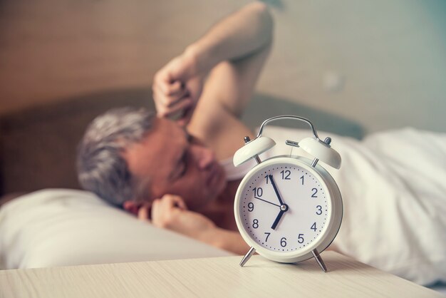 잠자는 남자 자명종 새벽을 방해. 침대에서 화난 사람은 소음으로 깨어났다. 일어났다. 오전 7시에 아침에 알람 시계를 끄는 침대에 누워있는 남자