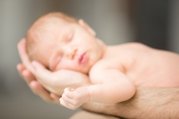 Sleeping newborn lying in male palms