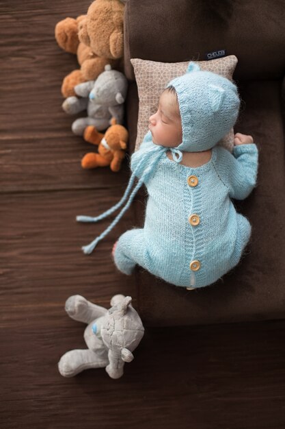 Sleeping newborn portrait of little baby boy in crocheted blue pijamas laying on brown little sofa