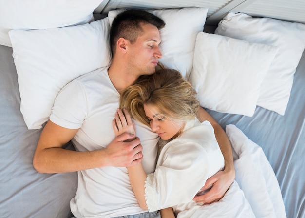 Sleeping young couple hugging on bed