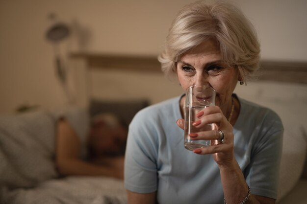 Sleepless mature woman having a glass of water in bedroom