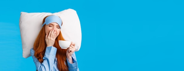 Foto gratuita sonnolenta ragazza europea dai capelli rossi con lunghi capelli rossi che indossa la maschera per il sonno degli indumenti da notte chiudi gli occhi e