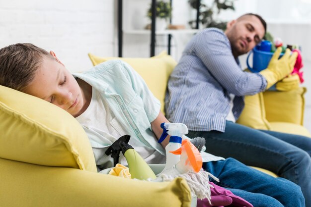 Sleepy father and son resting on sofa after cleaning