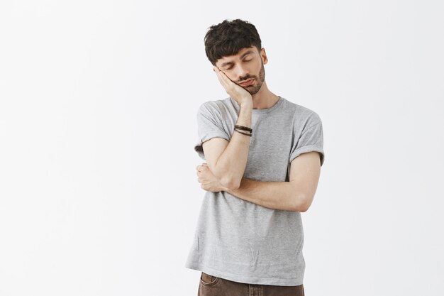 Sleepy handsome guy posing against the white wall