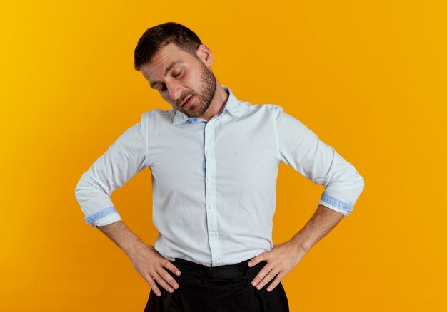 Sleepy handsome man puts hands on waist isolated on orange wall