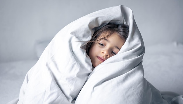 Sleepy little girl wrapped in a white blanket