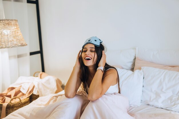 Sleepy woman waking up while sitting in bed on white wall