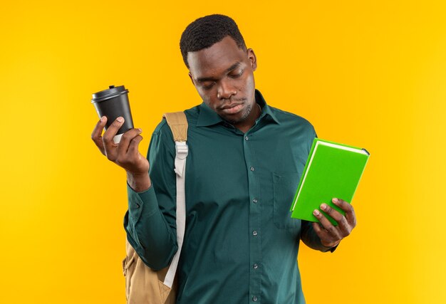 Sleepy young afro-american student with backpack holding book and paper cup