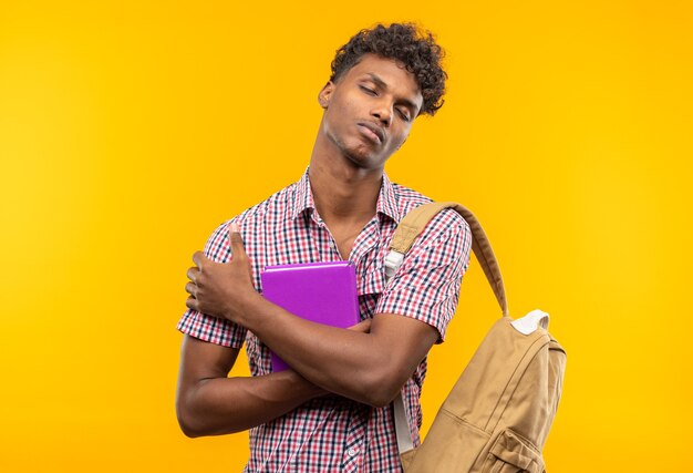 Sleepy young afro-american student with backpack holding book 