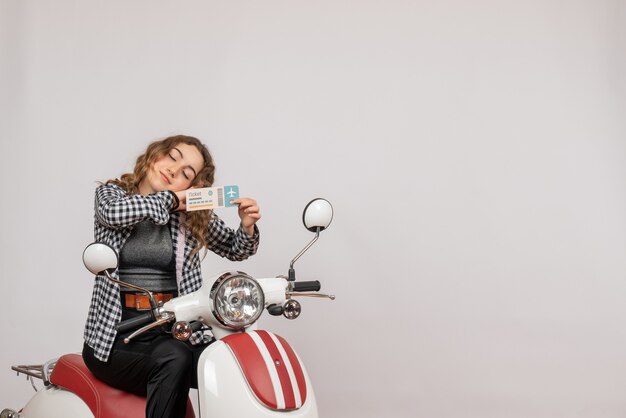 sleepy young girl on moped holding travel ticket on grey