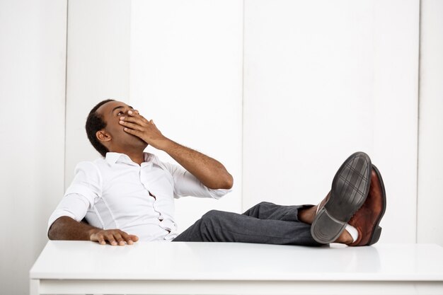 Sleepy young successful businessman yawning, sitting at workplace