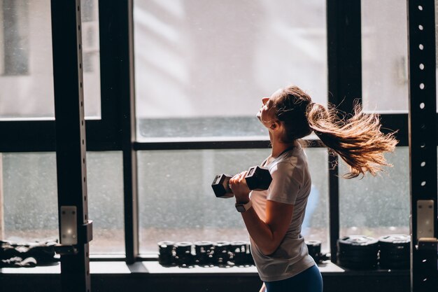 Slender athletic woman performs physical exercises with dumbbells