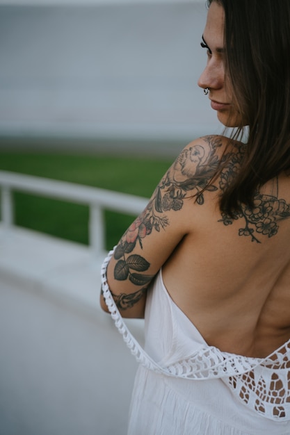 Foto gratuita snella donna sexy che mostra la sua schiena formosa in piedi in un abito bianco, guarda sopra la sua spalla