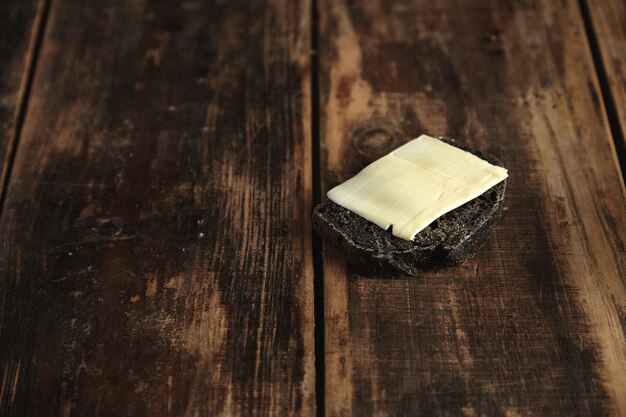 Slice of black charcoal luxury homemade bread with butter isolated on rustic wooden table