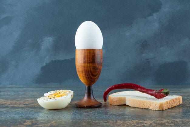 A slice of bread with boiled egg and chili pepper on marble background