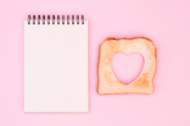 Slice of bread with cut out heart and notepad