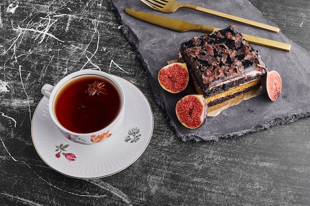 A slice of brownie cake with figs and a cup of tea. 