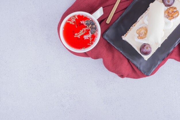 A slice of cake in a ceramic platter with a cup of red herbal tea.