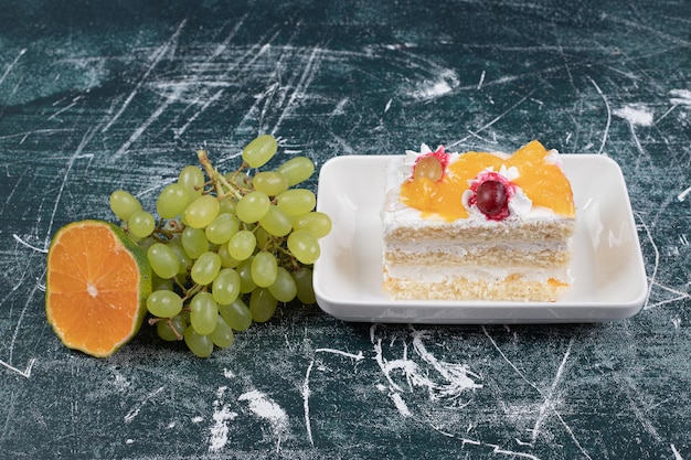 Slice of cake, grapes and orange on blue space. 