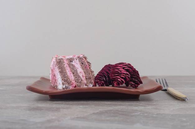 大理石のフォークの横にある大皿にケーキと赤い松ぼっくりのスライス