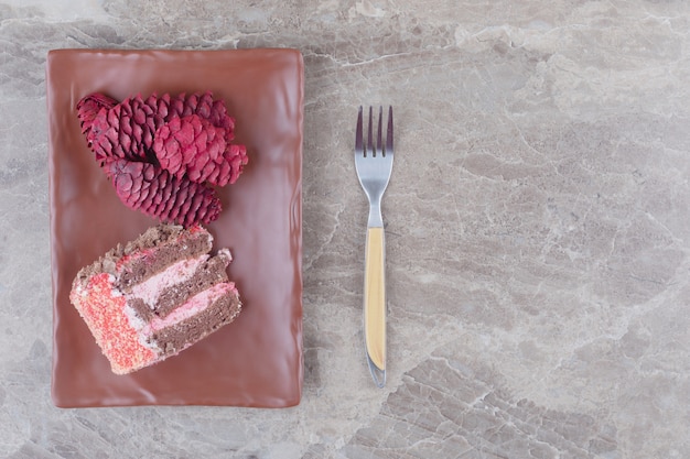 A slice of cake and red pine cones on a platter next to a fork on marble 