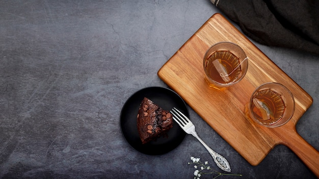 Free photo slice of cake and tea cups on a wooden support on a grey back ground