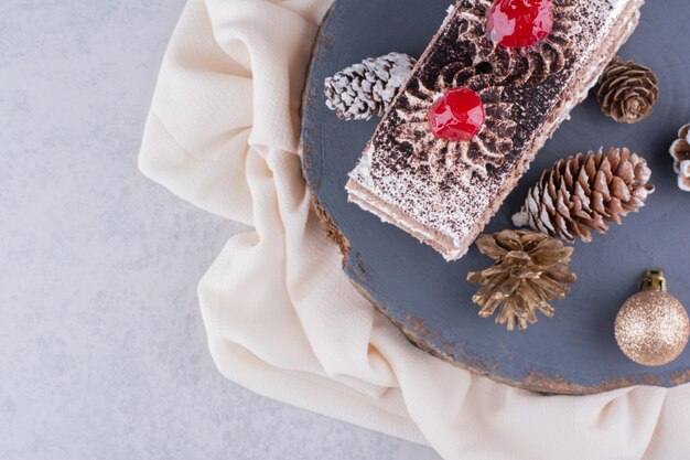 Slice of cake with Christmas ornaments on wood piece.