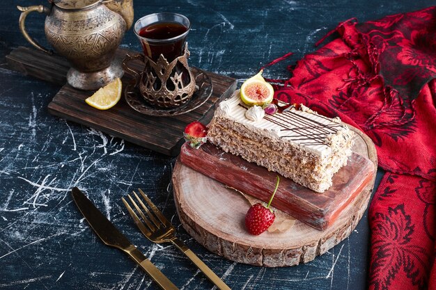 A slice of cake with a glass of tea on a wooden board. 