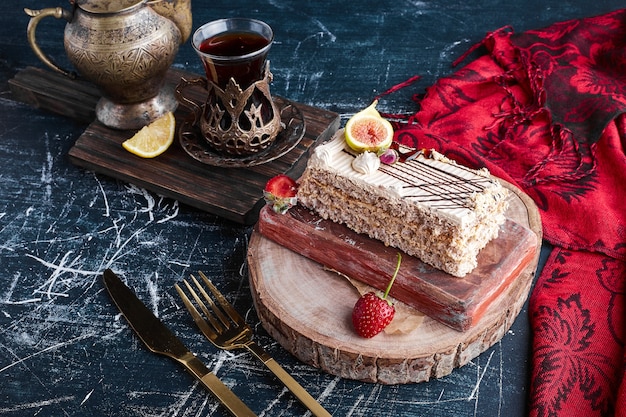 A slice of cake with a glass of tea on a wooden board. 
