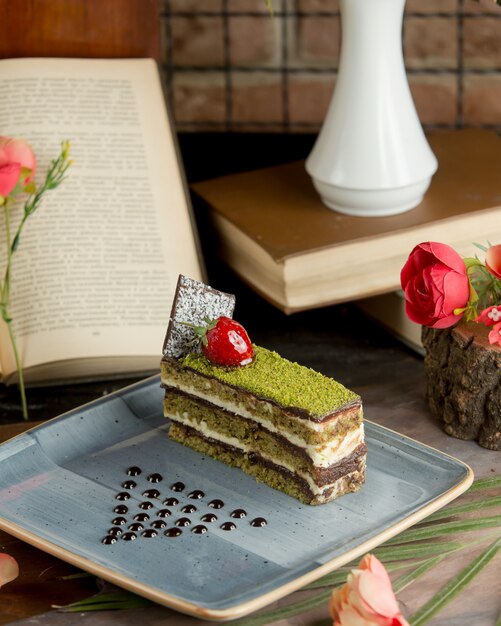 A slice of cake with minced pistachio and cherry berry.