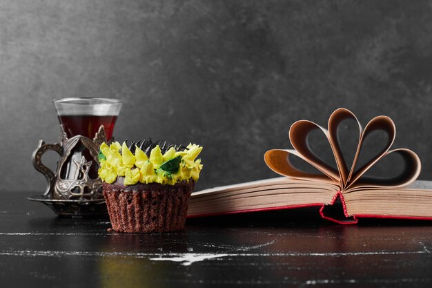 A slice of cake with sunflower cream decoration served with a glass of tea.