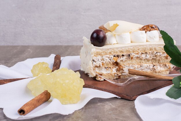 Slice of cake on wooden board with tablecloth and candies.