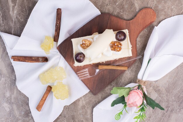 Slice of cake on wooden board with tablecloth and candies.