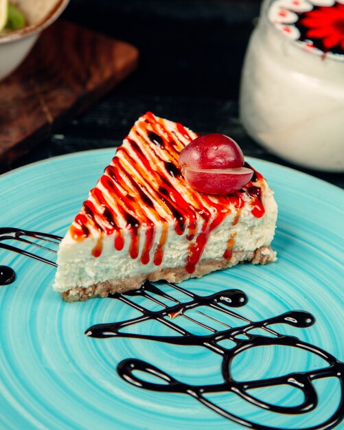 A slice of cheesecake with chocolate and strawberry syrup.