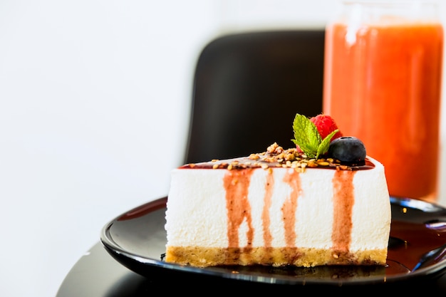 Slice of cheesecake with sauce and berries on black ceramic plate