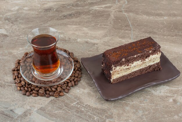 Slice of chocolate cake, coffee beans and glass of tea on marble table.