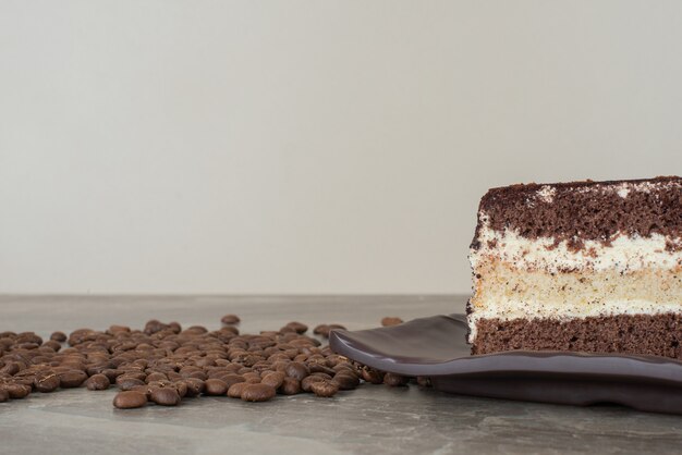 Slice of chocolate cake and coffee beans on marble table.