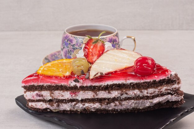 Кусочек шоколадного торта на тарелке с кусочками фруктов и чашкой чая.