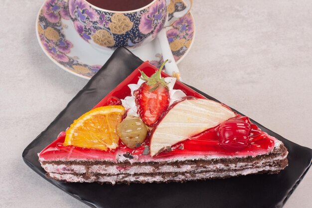 Slice of chocolate cake on plate with fruit slices and cup of tea.