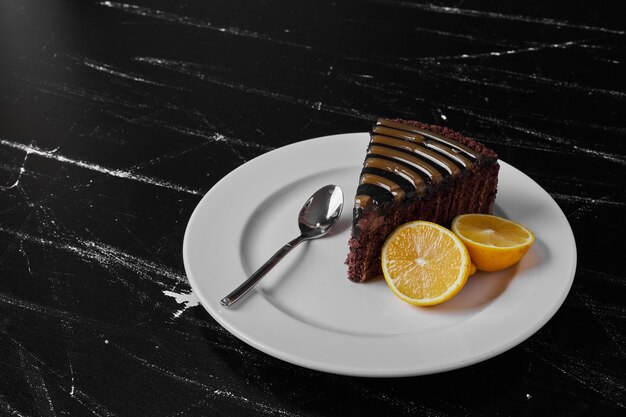 하얀 접시에 초콜릿 케이크 한 조각이 레몬과 함께 제공됩니다.