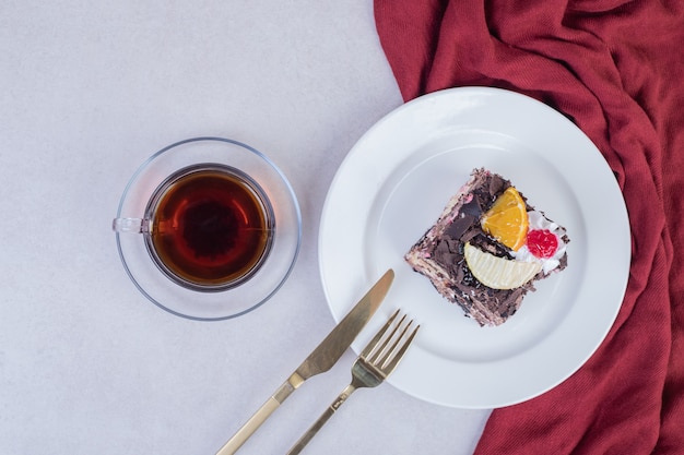 Slice of chocolate cake on white plate with cup of tea.